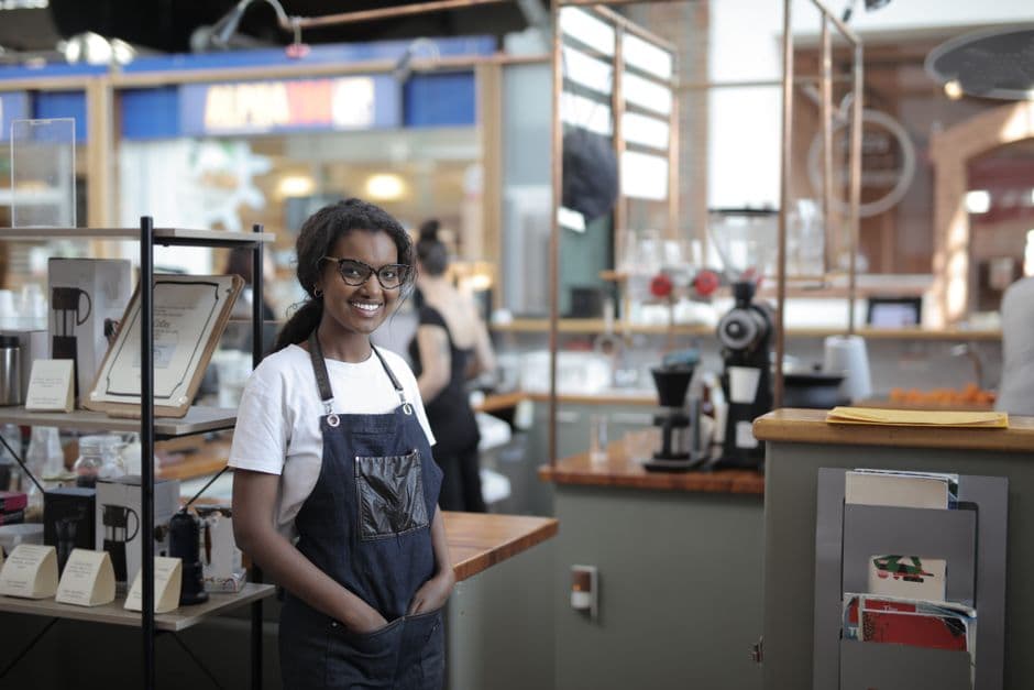 Smiling barista standing in a stylish café, showcasing entrepreneurial spirit.