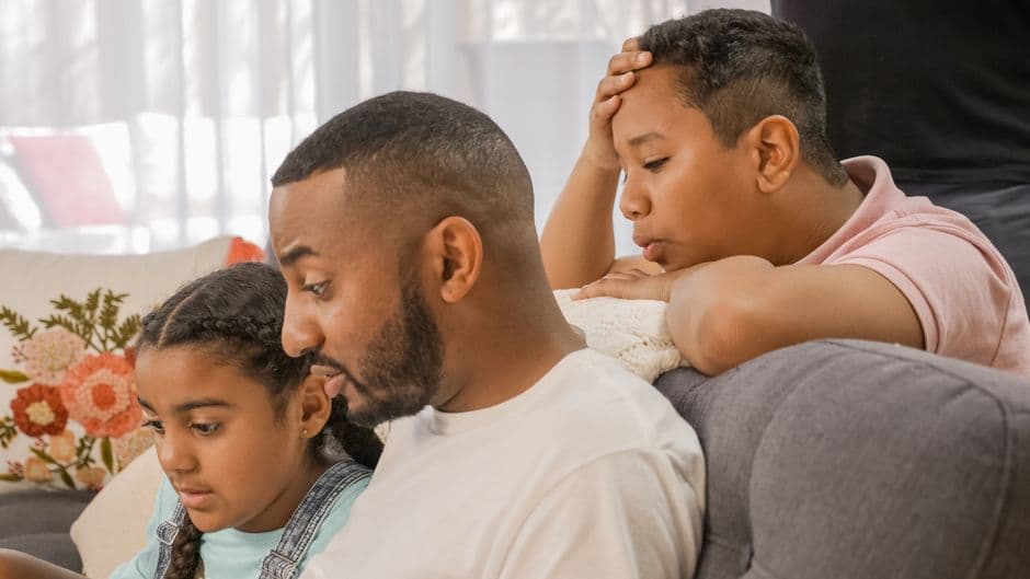 A father and his children engaged in an educational activity at home using a laptop.
