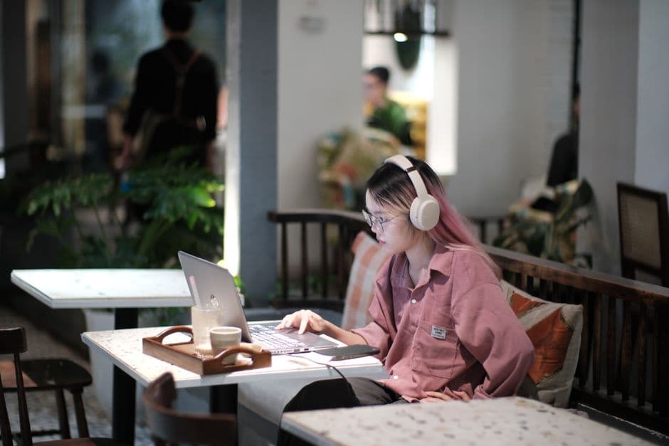 Woman with headphones working on laptop in a cozy Vietnamese cafe setting.