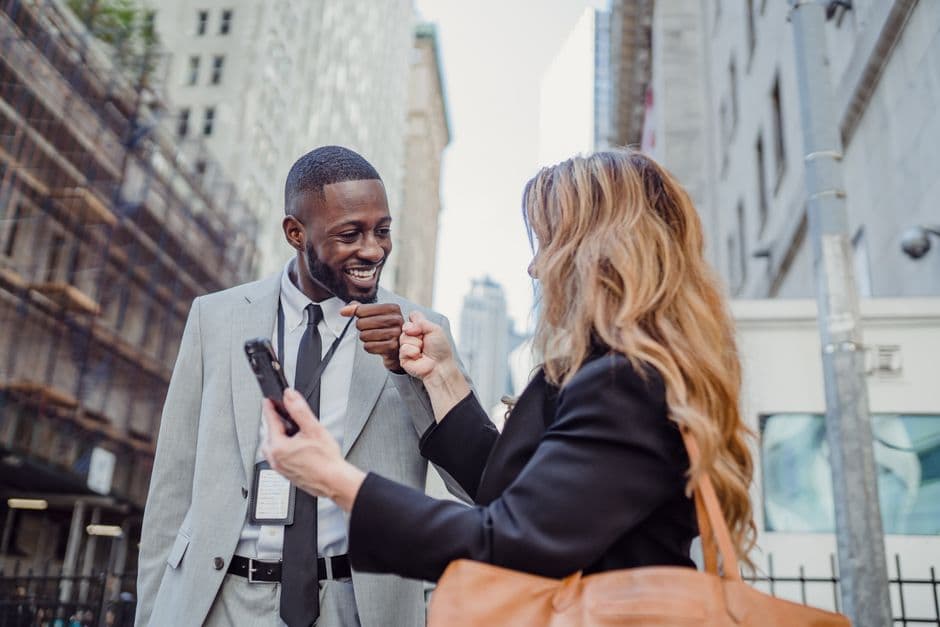 Businessman and businesswoman bumping fists in a city street, sharing a moment of success and camaraderie.