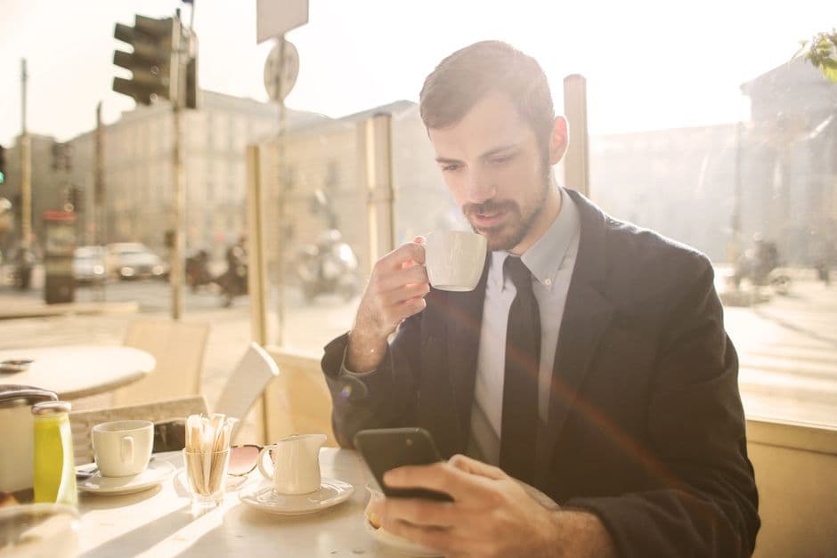 Businessman in a café enjoying coffee and using his smartphone on a sunny day.