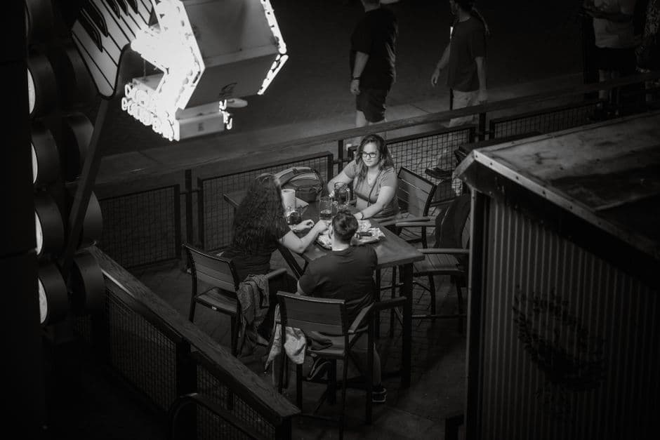 People dining under neon lights at night. Urban nightlife and social gathering captured in black and white.
