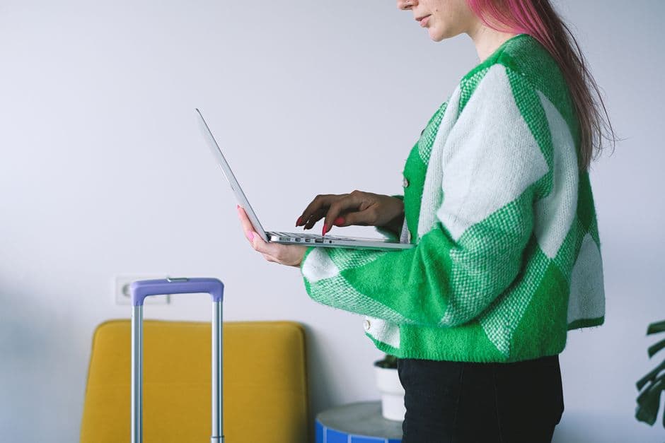 Young woman working on laptop near luggage in stylish hotel lounge, embracing the digital nomad lifestyle.