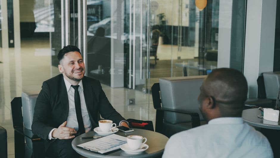 Two businessmen discuss plans over coffee in a modern indoor cafe setting.