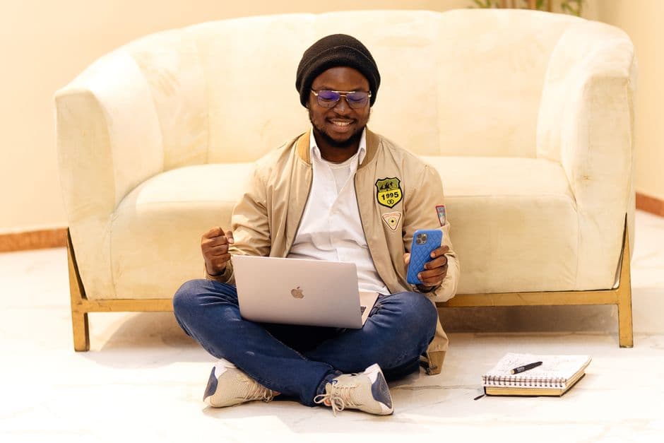 Smiling man in Lagos using laptop and smartphone, embodying modern remote work lifestyle.