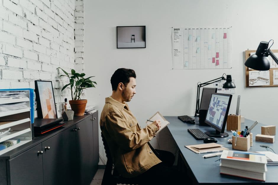 Young man in a brown jacket working at a computer in a stylish, modern office.