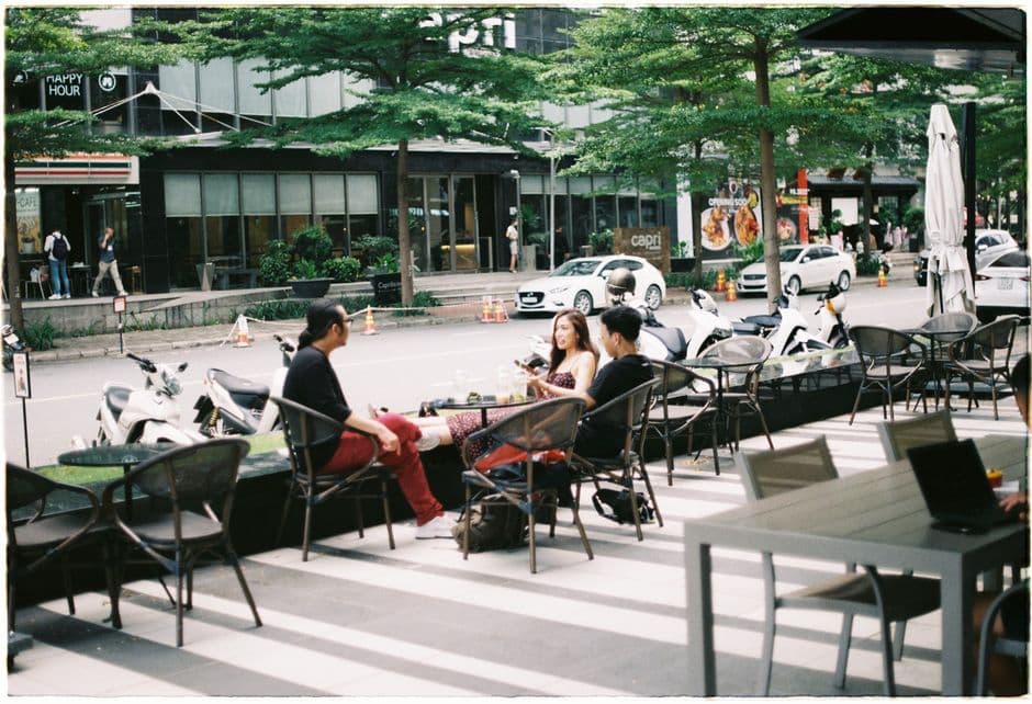Three young adults chatting at an outdoor cafe on a busy street.
