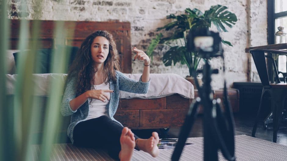 Woman sitting on floor filming vlog, discussing engaging topic. Home setting with cozy atmosphere.
