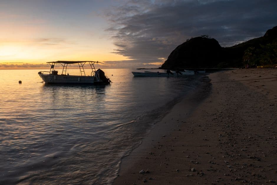 Serene sunrise over a tranquil Fijian beach with a boat, capturing a peaceful island life.